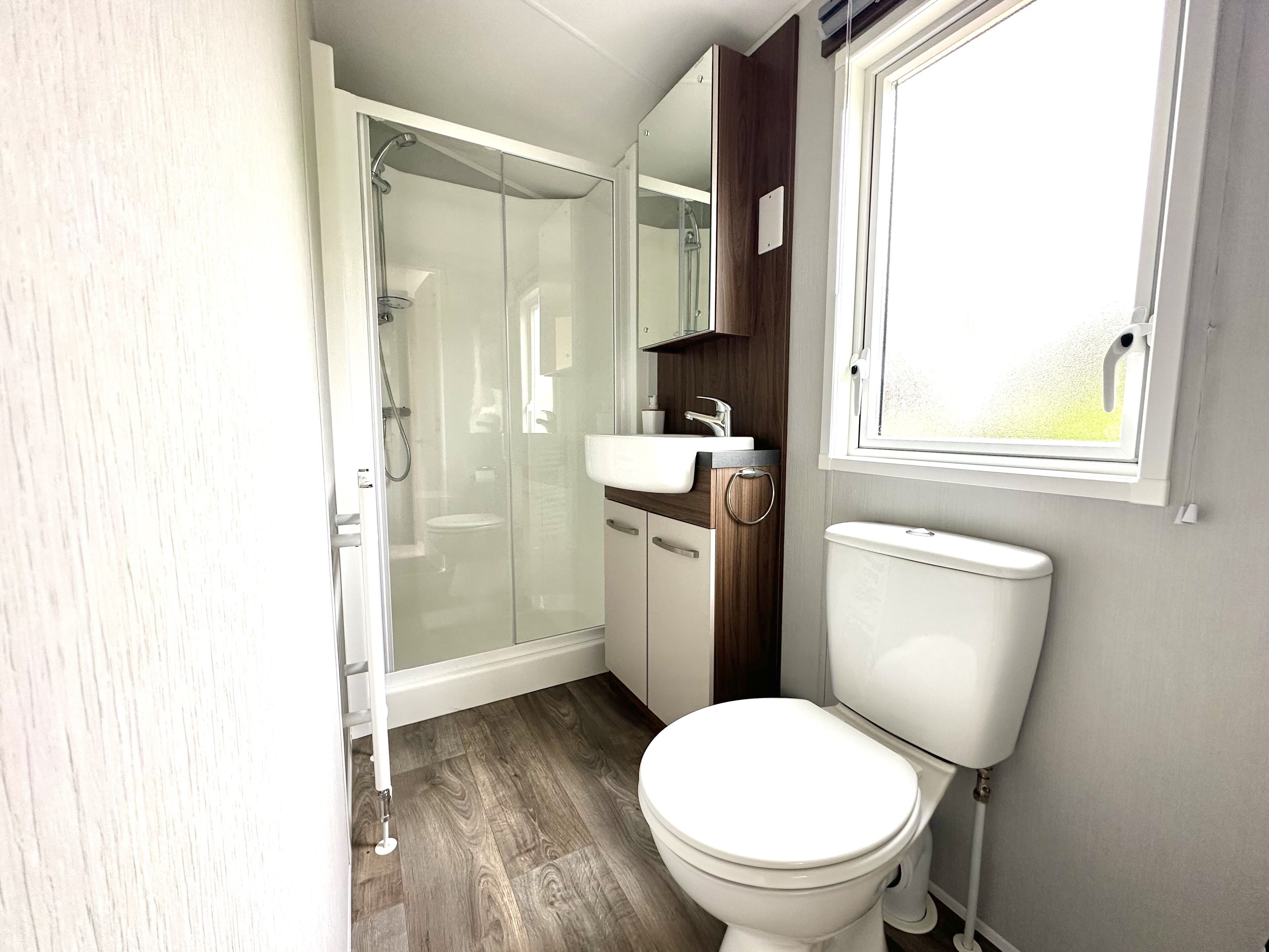 Un baño pequeño con cabina de ducha de vidrio, inodoro blanco y lavamanos.
