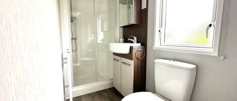 Un baño pequeño con cabina de ducha de vidrio, inodoro blanco y lavamanos.