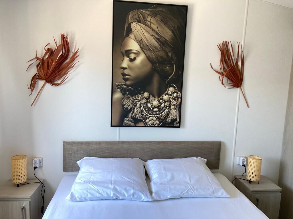 Une chambre à coucher avec un lit, des oreillers blancs, une tête de lit, deux tables de chevet avec des lampes et des œuvres d’art murales.