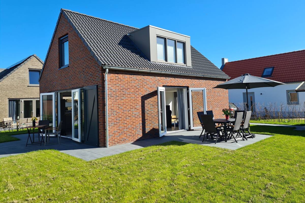 A modern house with a brick exterior, large windows, and a patio with outdoor furniture.
