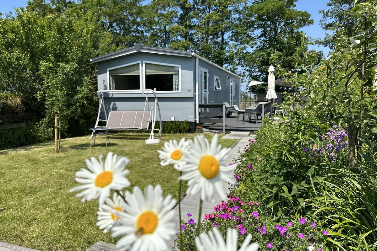 A mobile home with a patio area, a swing set, and a garden with flowers.
