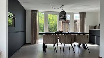 Een moderne keuken met een eethoek, grote ramen en een hangende lamp.