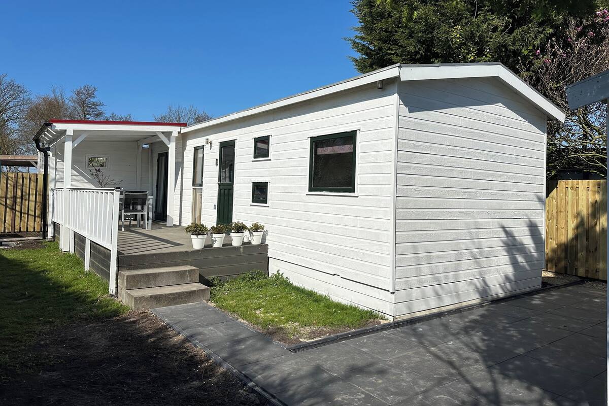 A single-story white house with a covered porch, a small front yard, and a wooden fence.