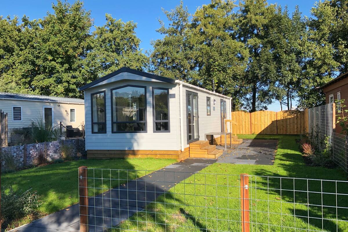 A mobile home with a large window, a small porch, and a fenced yard.