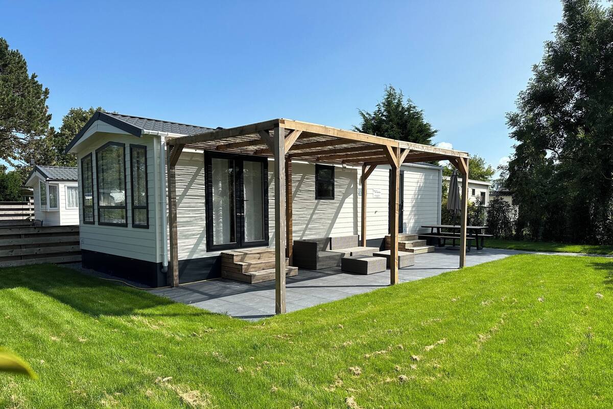 A mobile home with a covered patio area, a small deck, and a grassy yard.