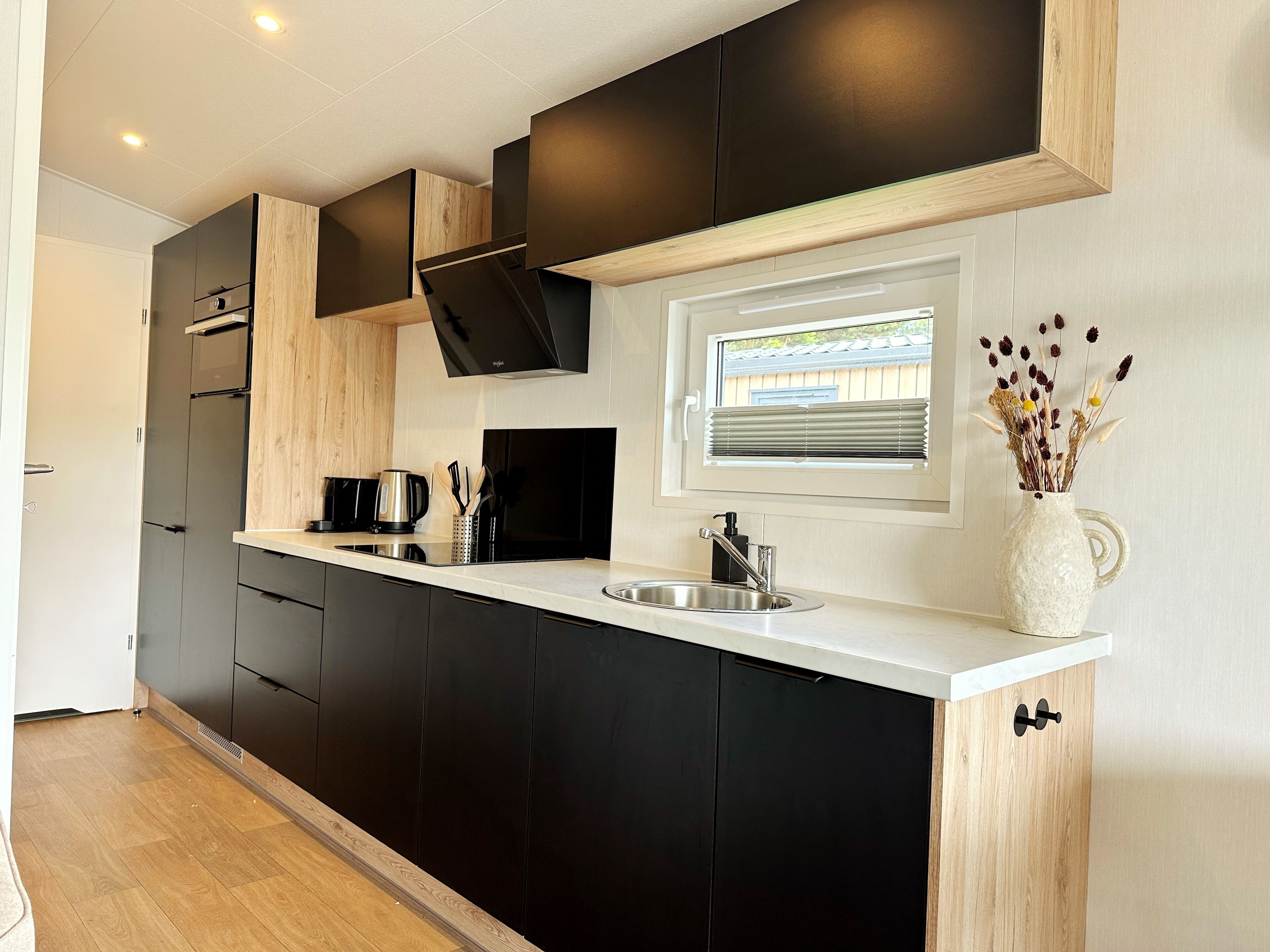 A modern kitchen with black cabinets, a white countertop, a built-in oven, and a window with blinds.