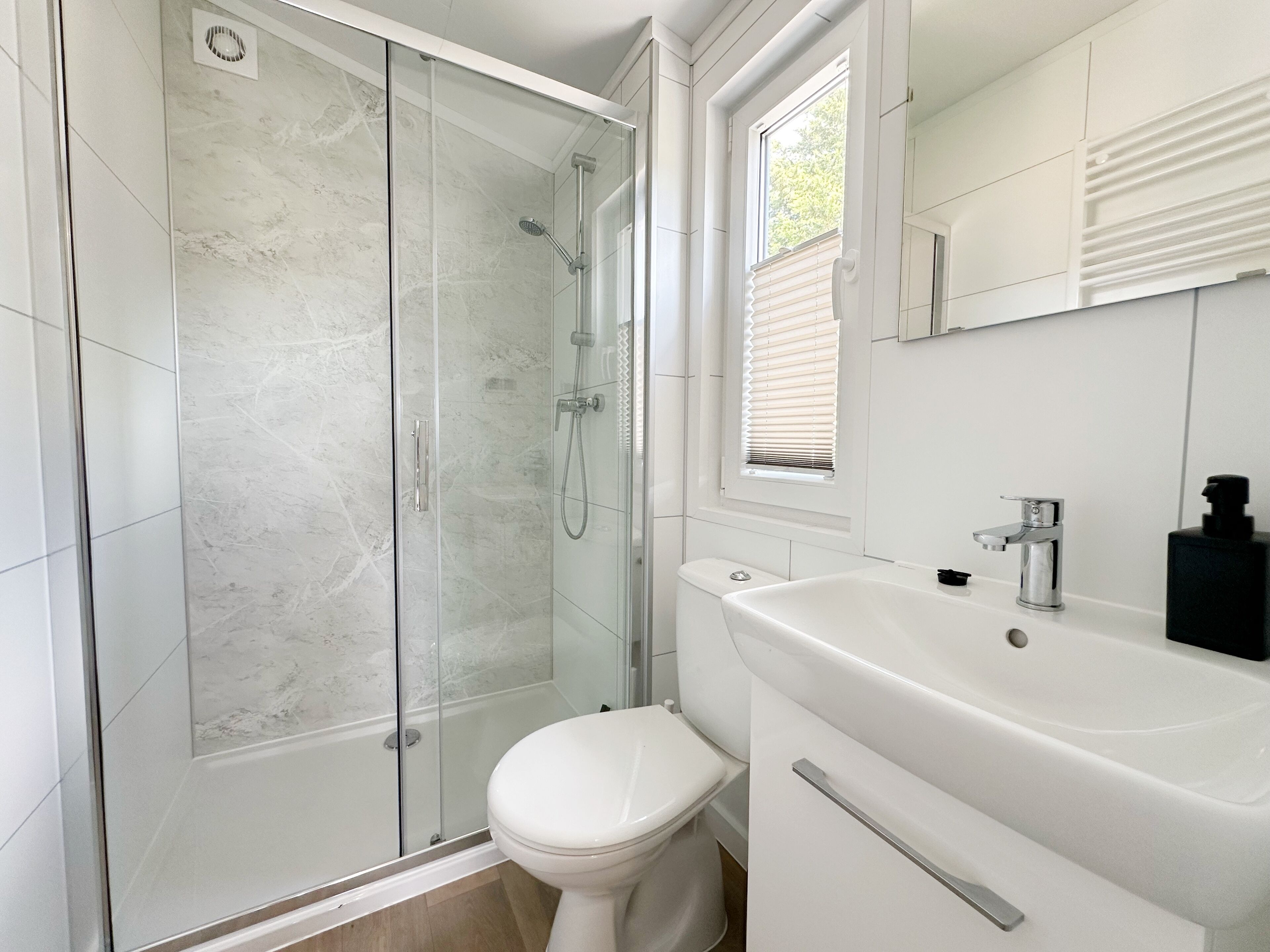 Un baño moderno con ducha de vidrio, inodoro blanco y lavamanos con espejo.