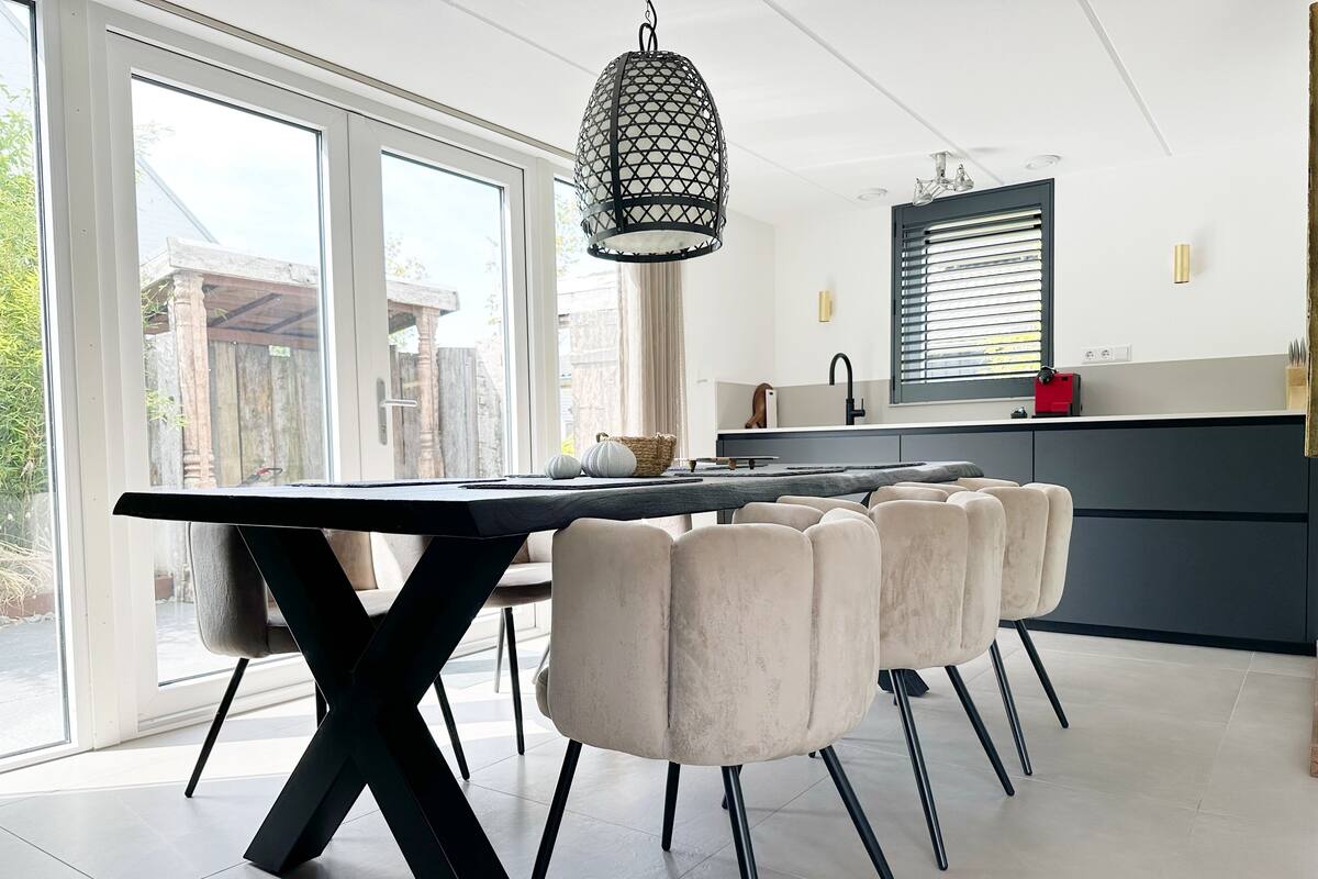 A modern kitchen with a large dining table, a hanging light fixture, and a view of the outside.