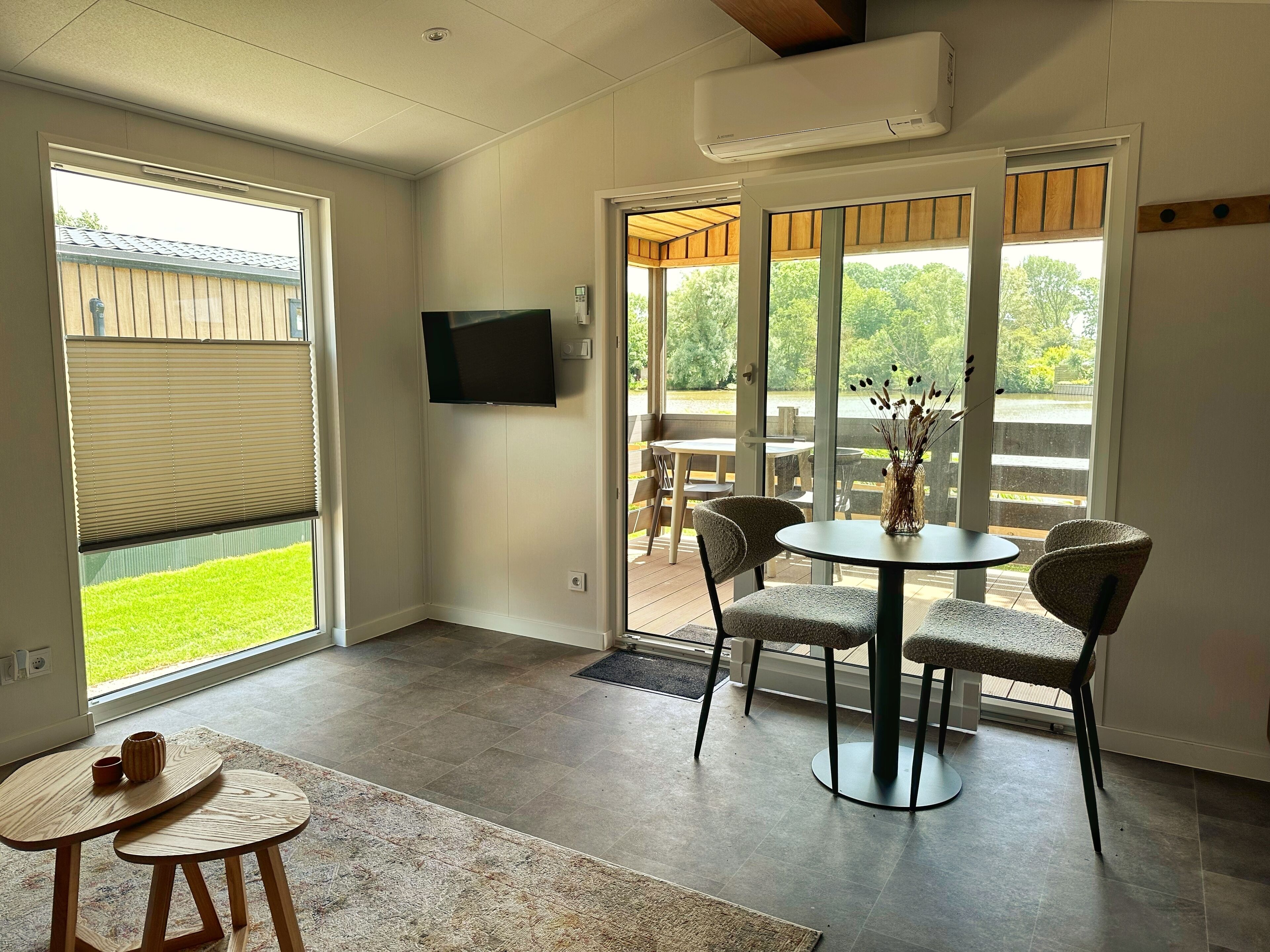 A modern room with a sliding glass door leading to an outdoor area, a round table with chairs, and a flat-screen TV mounted on the wall.