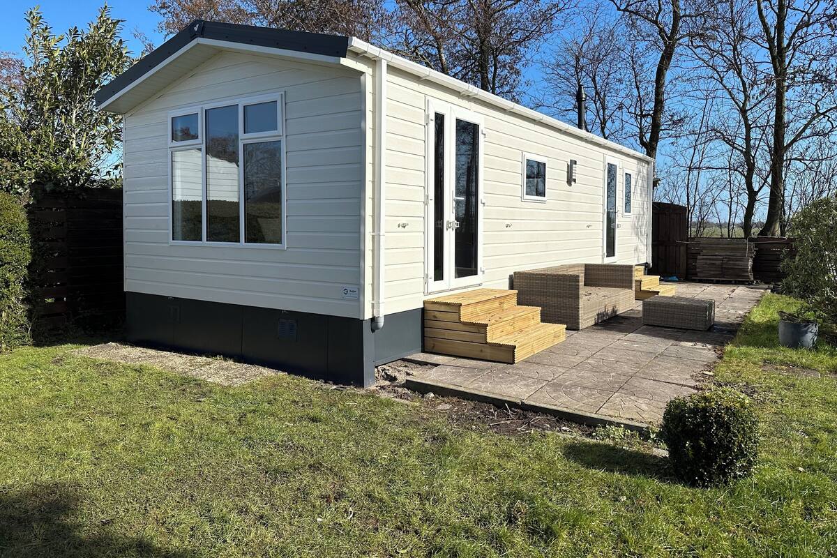 A single-story mobile home with a front porch, a small deck, and a fenced backyard.