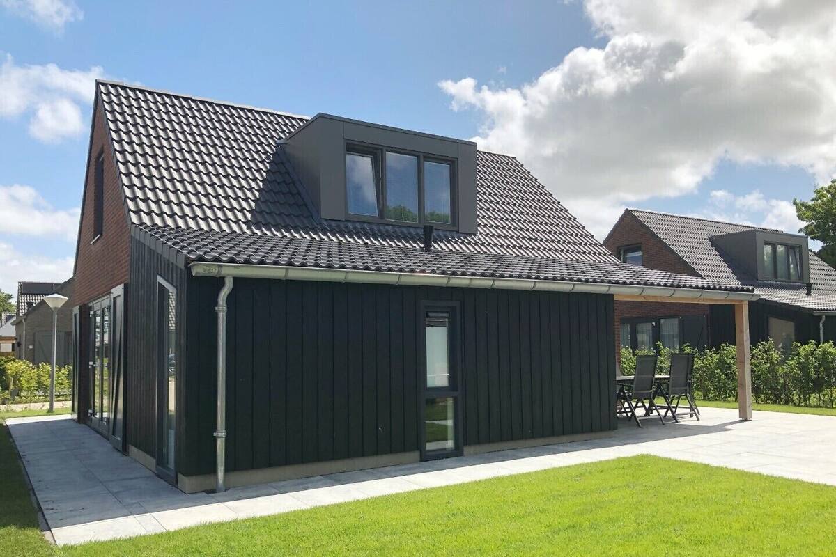 A modern house with a sloped roof, large windows, and a covered patio area.