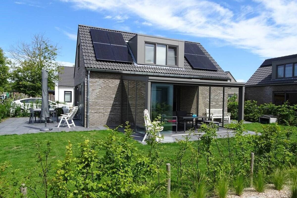 A modern house with a sloped roof, solar panels, a glass door entrance, and a patio with outdoor furniture.