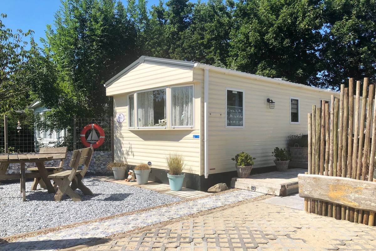 A mobile home with a covered porch, a dining table, and potted plants.