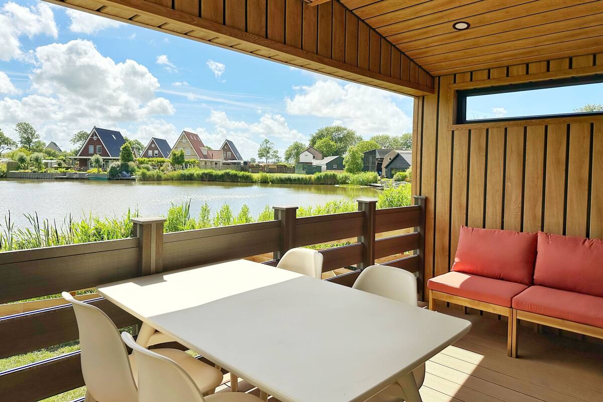 A wooden deck with a table and chairs, a red sofa, and a view of houses across a lake.