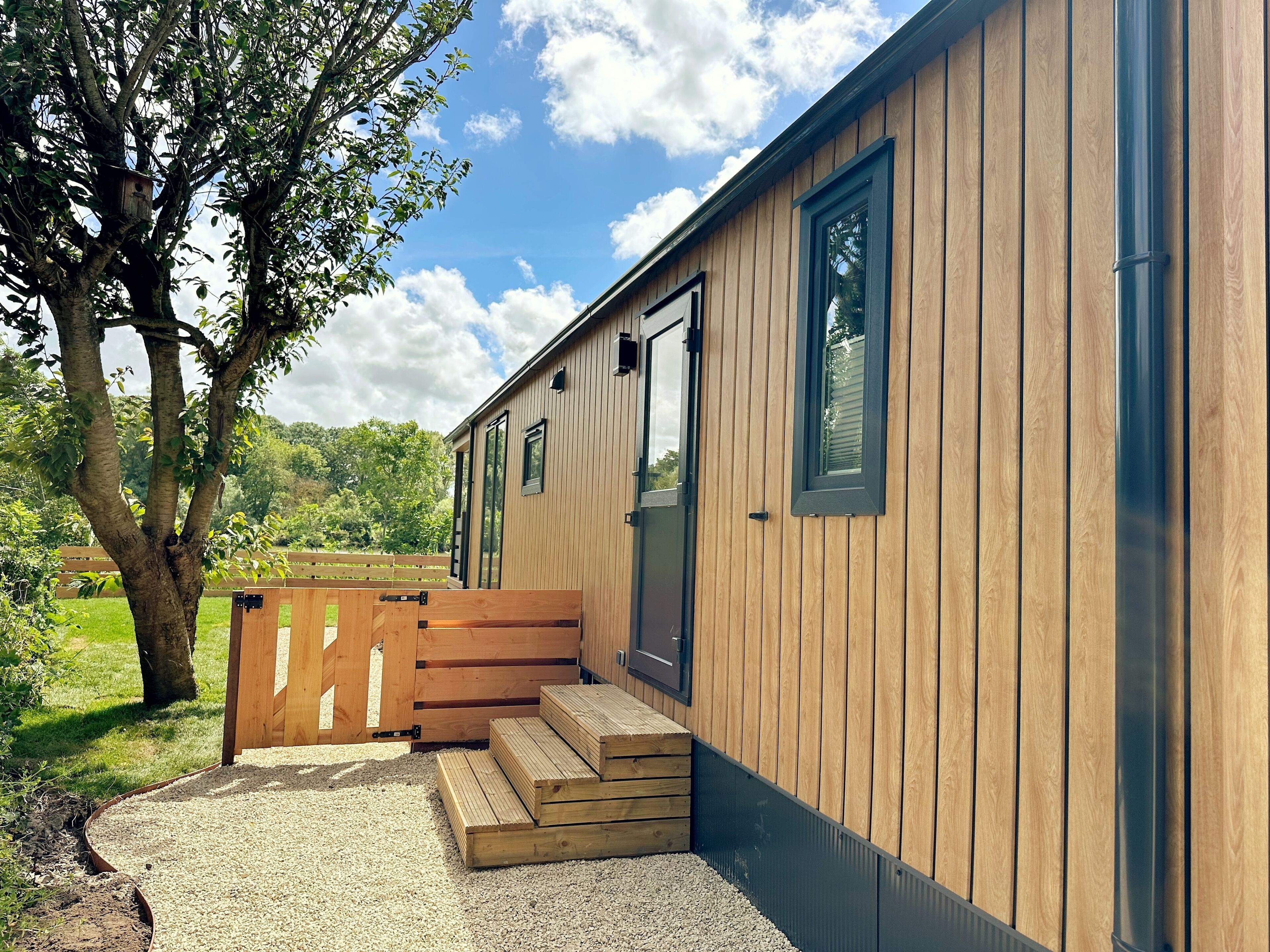 Een houten chalet met een voordeur, ramen en een klein terras met treden erheen.