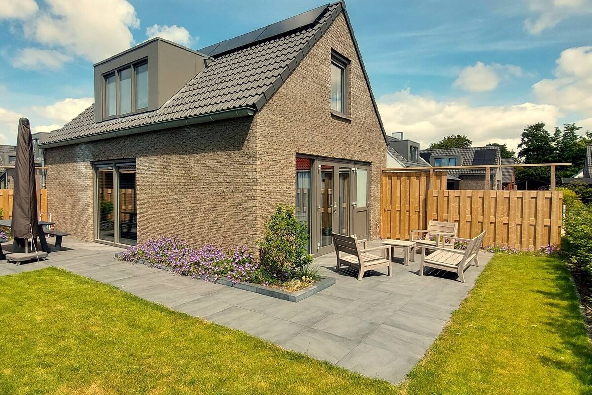 A modern house with a sloped roof, large windows, and a patio with outdoor furniture.