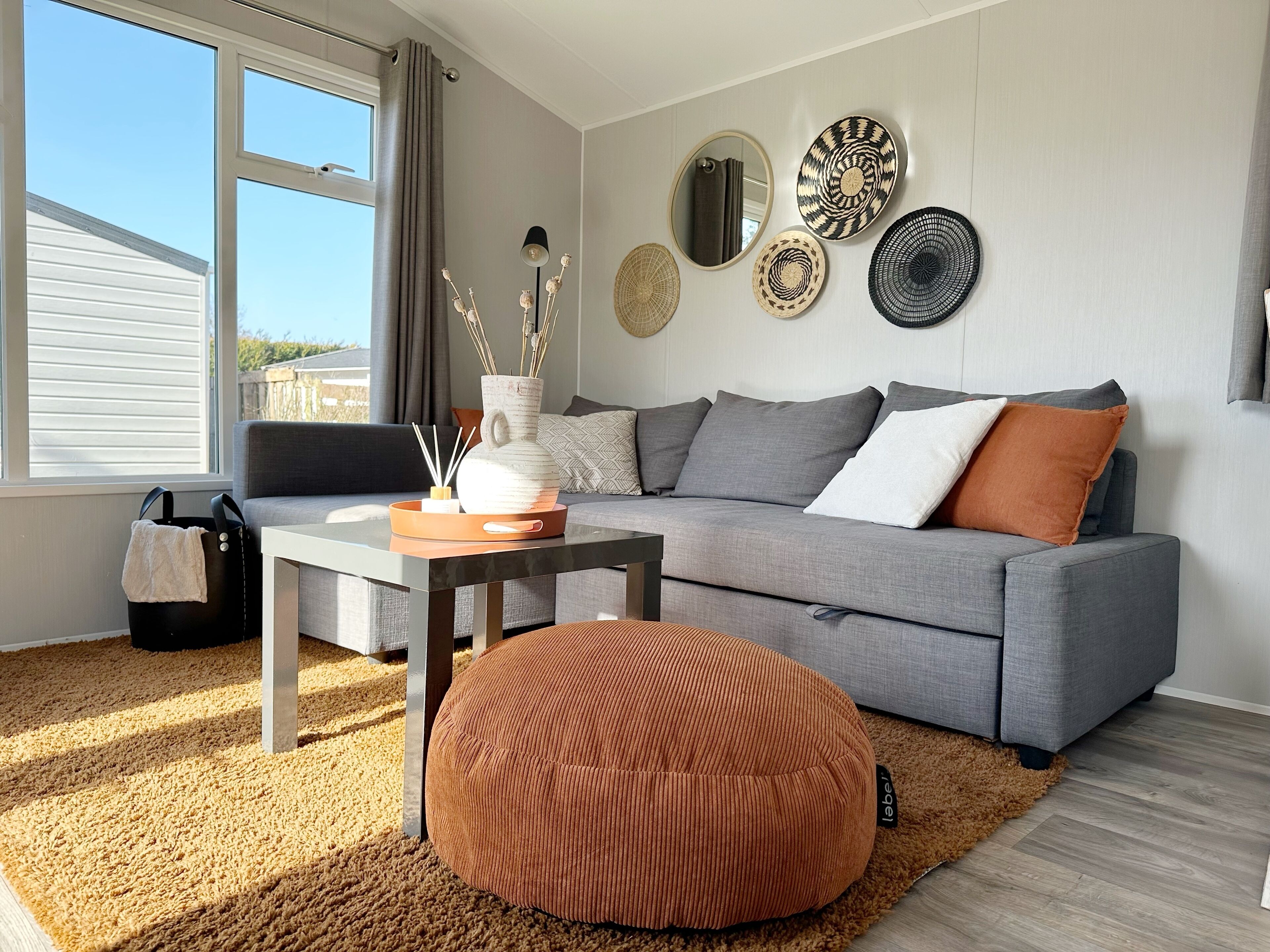 Un salon moderne avec un canapé gris, un pouf rond, une table basse et des assiettes décoratives accrochées au mur.