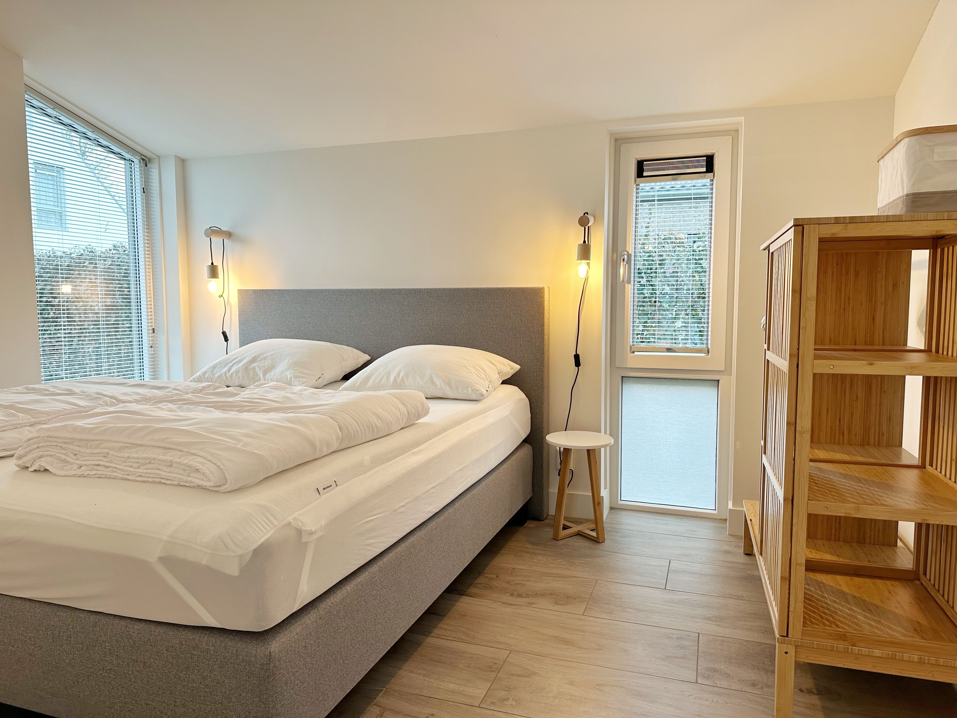 A neatly made bed with white linens, a grey headboard, and two bedside lamps.