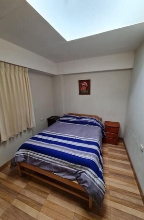 A bedroom with a bed, a nightstand, a small cabinet, a window with curtains, and a skylight. - Ukumary Gosth (Cusco)