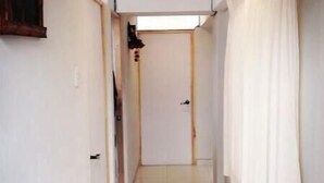A narrow, tiled hallway with white walls and a door at the end. - Ukumary Gosth (Cusco)