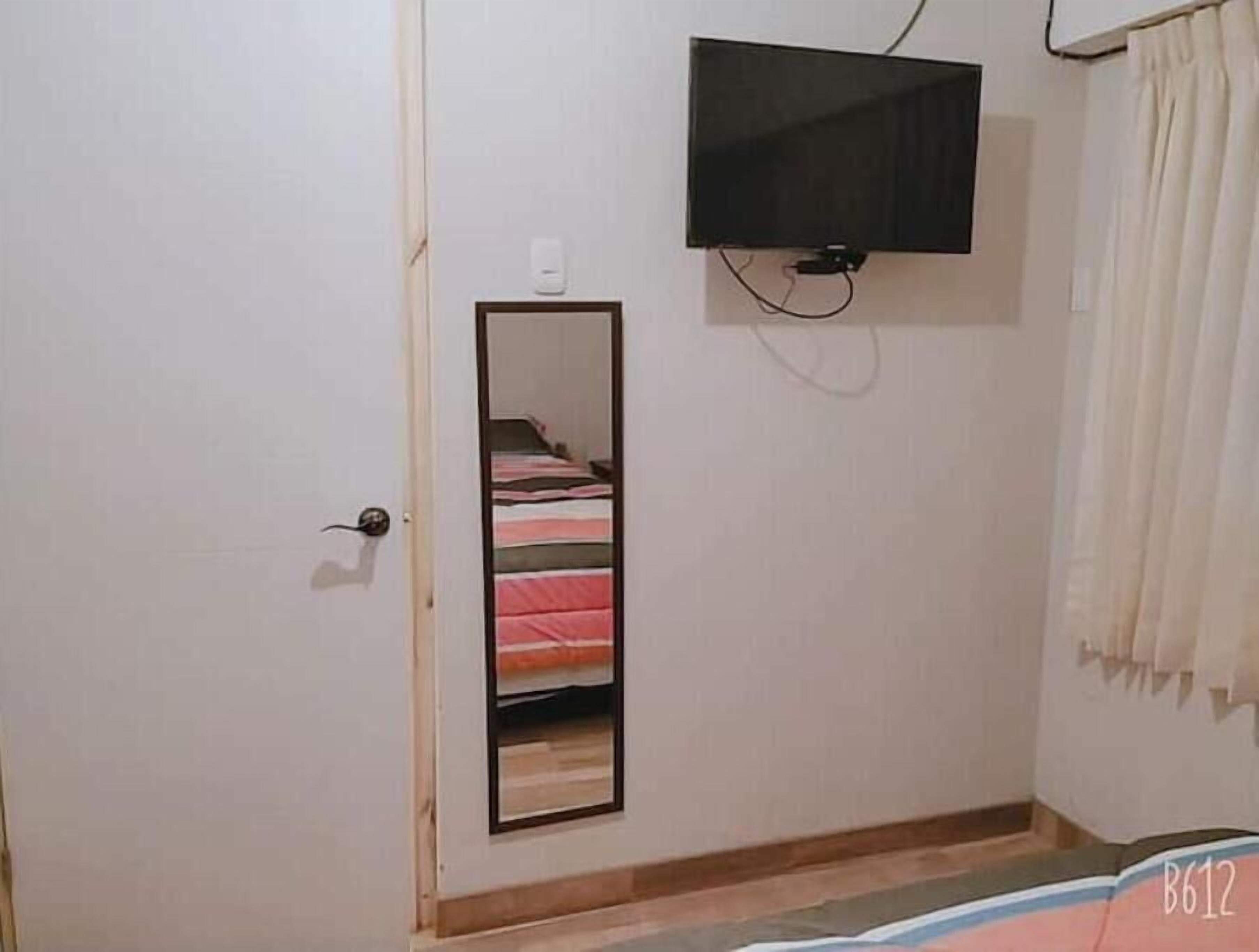 Een slaapkamer met een bed, een aan de muur bevestigde televisie, een spiegel en een deur.