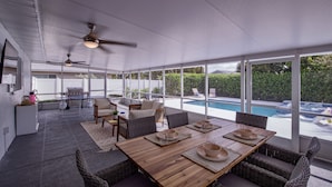 Un espace extérieur abrité, aménagé pour les repas, avec vue sur la piscine, doté de mobilier en osier et de ventilateurs de plafond.