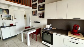 Una cocina compacta con armarios blancos, una silla roja, una mesa de comedor y una cafetera roja.