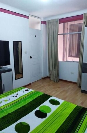 Una habitación con cama, escritorio, espejo, ventana con cortinas y puerta.