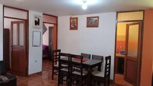 Zona pranzo con tavolo e sedie in legno, pavimento piastrellato e lampada a soffitto.