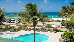 Ein Poolbereich mit Liegestühlen und Sonnenschirmen, ein Strand mit Autos und Menschen sowie ein Blick auf das klare, blaue Meer.