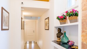 Un pasillo decorado con un cuadro, un busto y plantas en macetas.