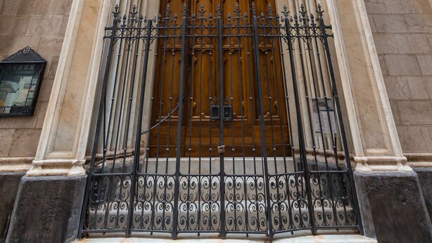 Fachada de iglesia con una puerta de madera grande, arcos apuntados y una reja de hierro forjado negro.