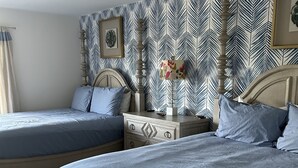 A bedroom with two beds, a dresser, a nightstand, and a patterned wallpaper. - Beautiful Key Largo Bayside Condo! (Key Largo)