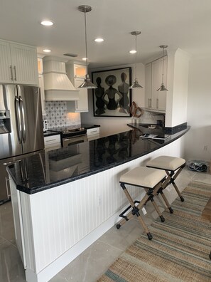 A modern kitchen with white cabinetry, stainless steel appliances, a black granite countertop, and pendant lighting. - Beautiful Key Largo Bayside Condo! (Key Largo)