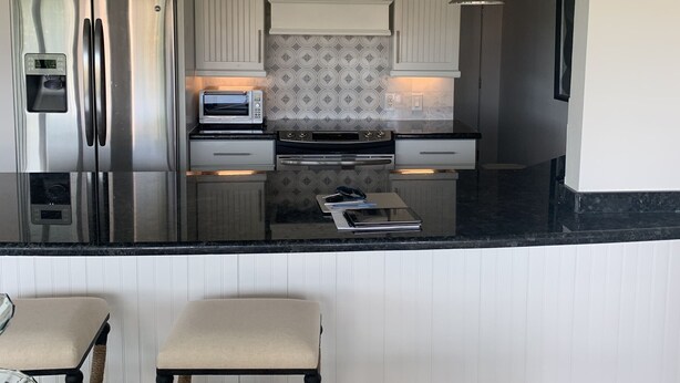 A modern kitchen with white cabinetry, stainless steel appliances, and a black countertop. - Beautiful Key Largo Bayside Condo! (Key Largo)