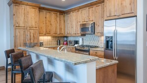 A kitchen with wooden cabinets, a stainless steel refrigerator, a microwave, a stove, and a bar area with chairs. - Ski-in/out luxury condo. Best in the complex. Outdoor pool and hot tubs!! (Bachelor Gulch)
