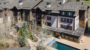 A large, multi-story house with a prominent swimming pool, surrounded by trees and mountains. - Ski-in/out luxury condo. Best in the complex. Outdoor pool and hot tubs!! (Bachelor Gulch)