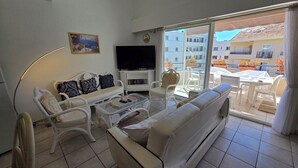 A living room with a sofa, chairs, a coffee table, a TV, and a balcony with outdoor furniture. - Appartement 3 Pièce Climatisé, Centre Ville de Sainte-maxime (Sainte-Maxime)