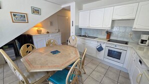 A compact kitchen with white cabinets, a dining table with chairs, a stove, and a sink. - Appartement 3 Pièce Climatisé, Centre Ville de Sainte-maxime (Sainte-Maxime)