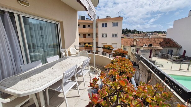 A balcony with a table and chairs, potted plants, and a view of a swimming pool and buildings. - Appartement 3 Pièce Climatisé, Centre Ville de Sainte-maxime (Sainte-Maxime)
