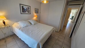 Quarto com uma cama, duas luminárias de cabeceira e uma porta que dá para outro espaço.