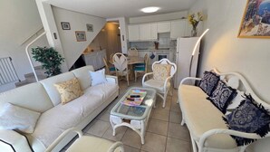 A living room with a sofa, chairs, a coffee table, and a kitchen in the background. - Appartement 3 Pièce Climatisé, Centre Ville de Sainte-maxime (Sainte-Maxime)