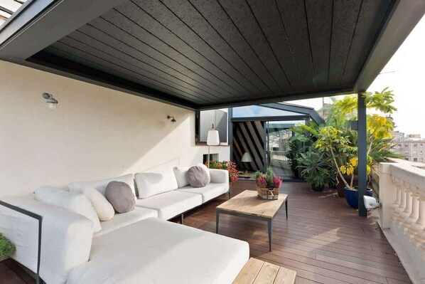 A modern outdoor living area with a white sofa, a wooden coffee table, and potted plants.