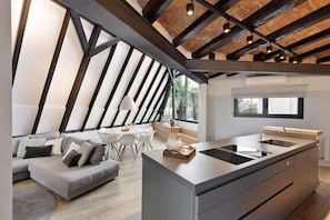 A modern kitchen with a central island, a dining area with a white table and chairs, and a cozy seating area with a grey sofa.