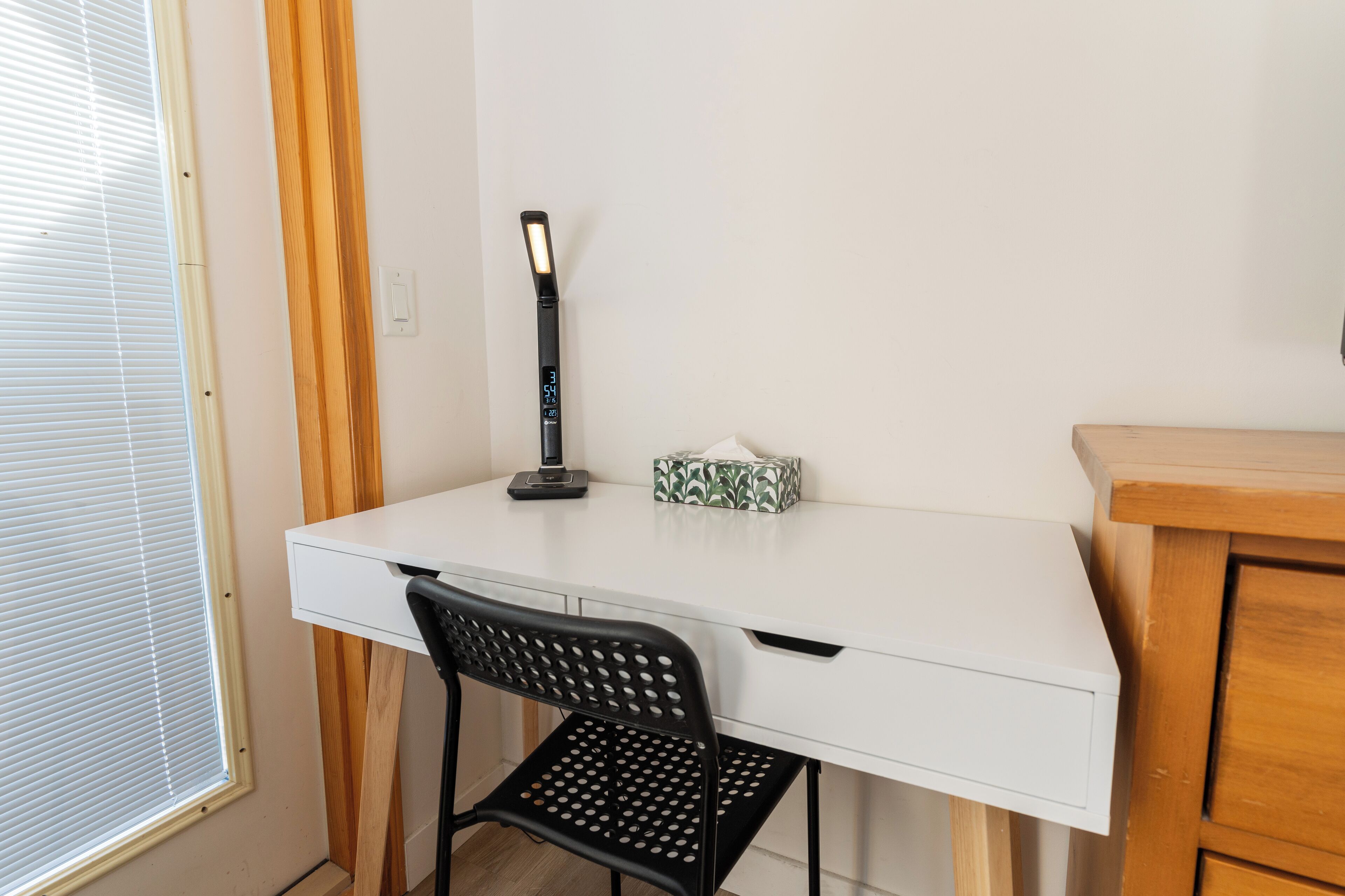 Un escritorio blanco con una silla negra, una lámpara y una caja de pañuelos.