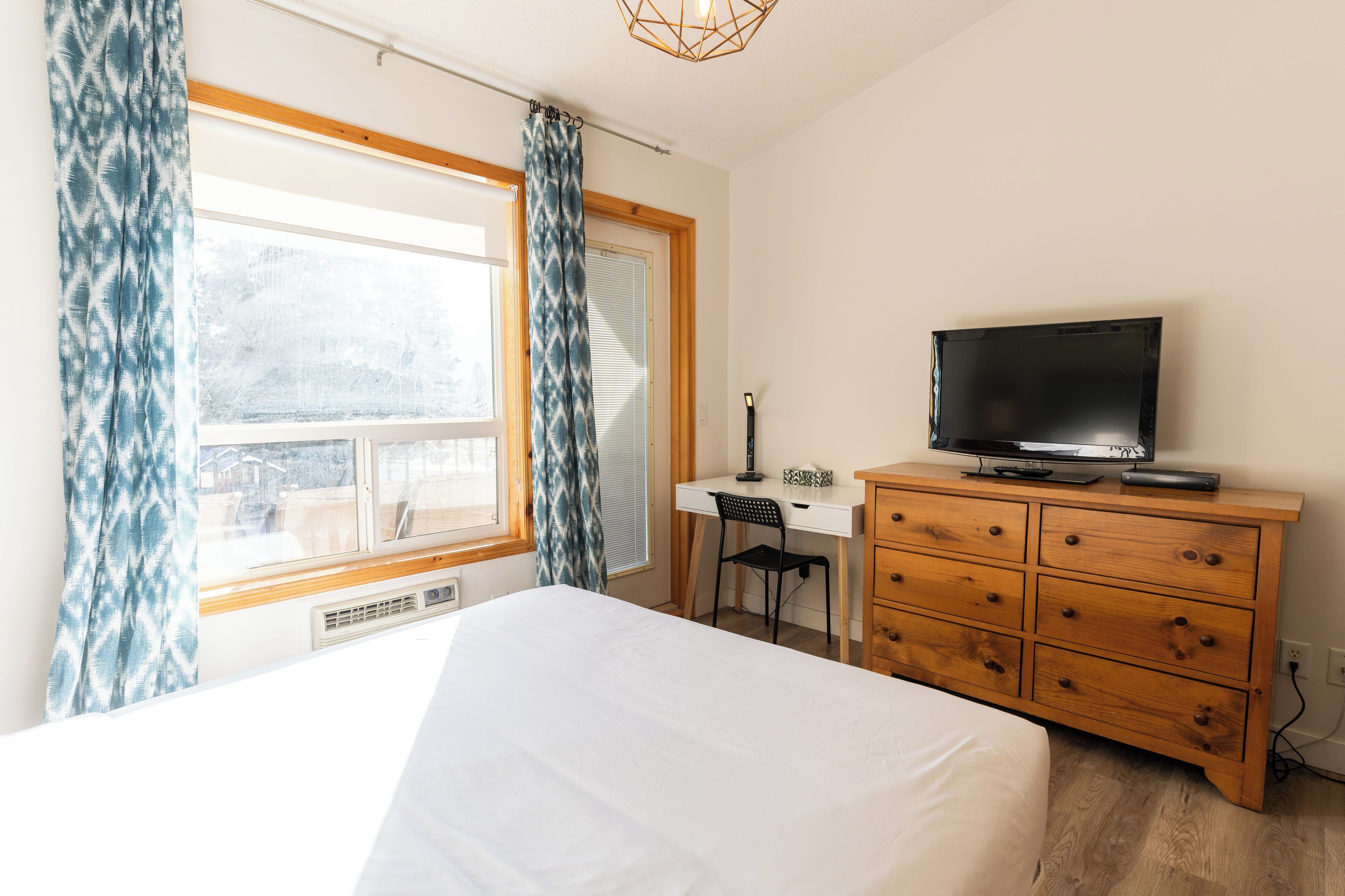 A bedroom with a bed, a desk, a television, and a dresser.