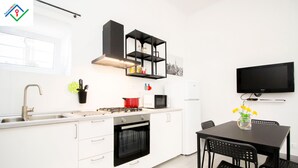 Moderni keittiö, jossa on valkoiset kaapit, sisäänrakennettu uuni, mikroaaltouuni ja musta televisio, joka on kiinnitetty seinään.