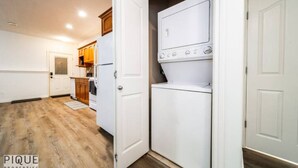 Un lavadero con lavadora y secadora, armarios de madera y una puerta que da a otra habitación.