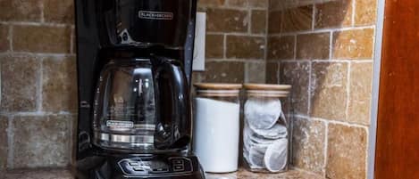 A black coffee maker on a granite countertop with a stone backsplash.