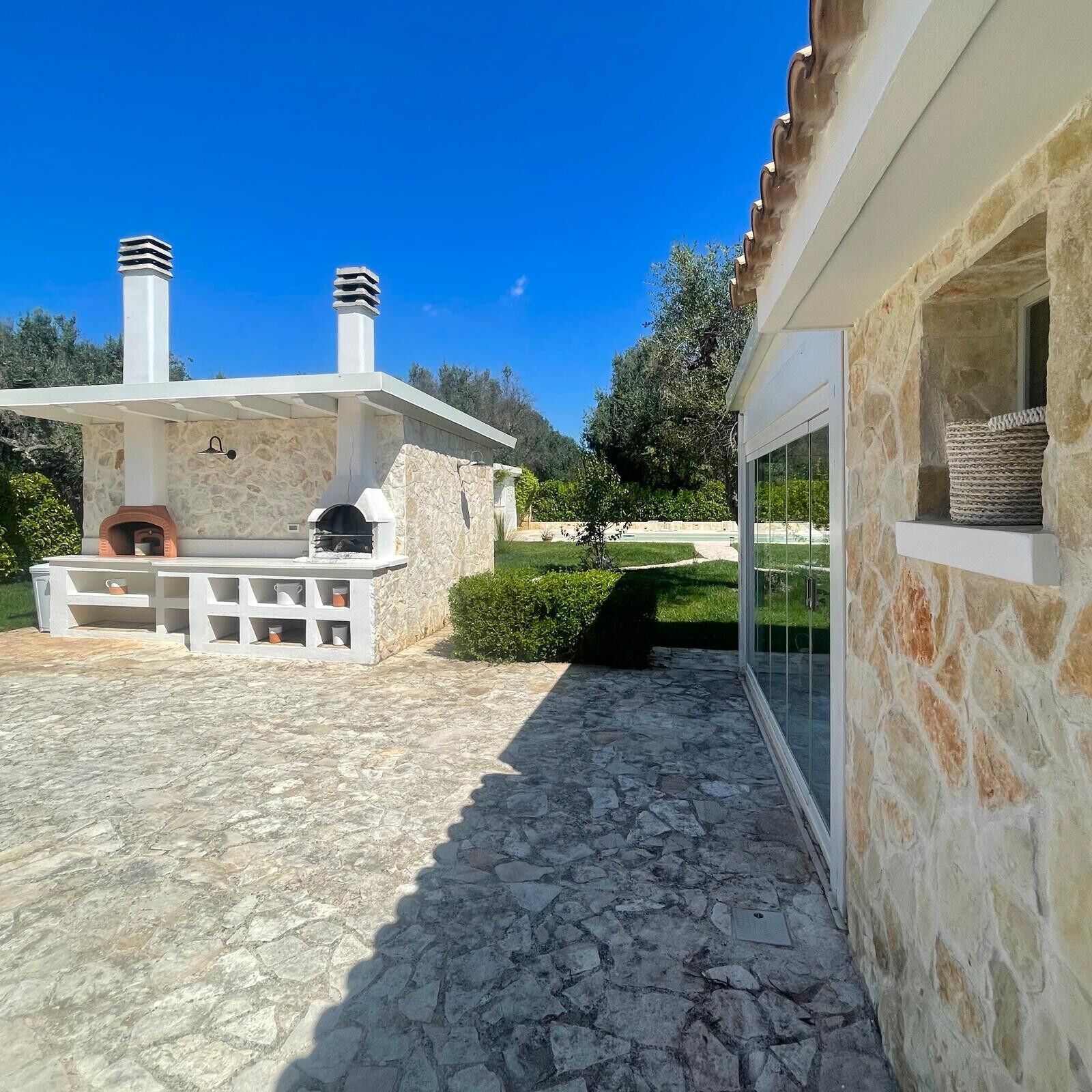 Un patio de piedra con zona de barbacoa, un edificio de piedra con chimenea y una ventana con cestas.